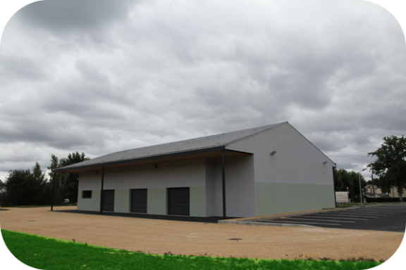 Bâtiment moderne en métal avec un toit surplombant, sous un ciel nuageux.