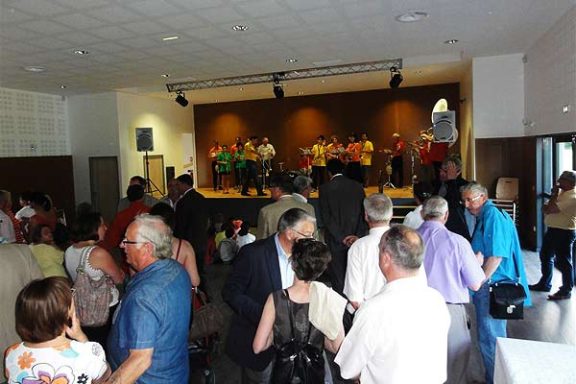 Spectacle dans une salle animée, avec des personnes sur scène et un public attentif.